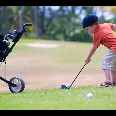 Criança a jogar golfe num campo verde com carrinho de golfe ao lado