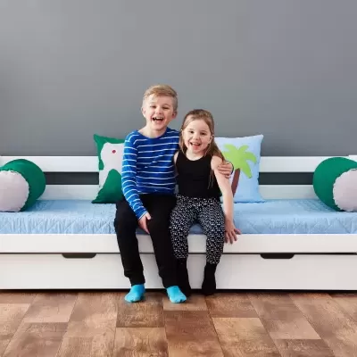 Cama branca em madeira com gaveta, colchão azul e almofadas decorativas com crianças sentadas