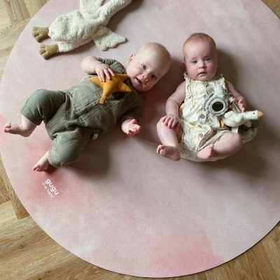 Dois bebés num tapete redondo cor-de-rosa com brinquedos de peluche
