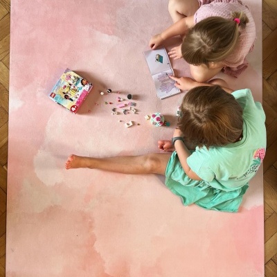 Tapete de brincar rosa com crianças sentadas e brinquedos pequenos