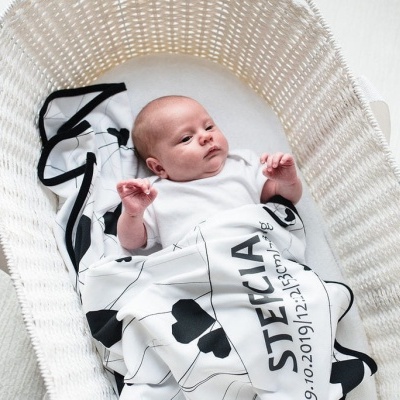 Bebé num berço branco com manta branca e preta com texto