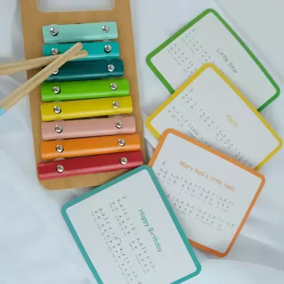 Xilofone colorido com cartões musicais em fundo branco.