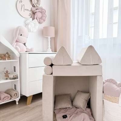 Quarto infantil com tenda de tecido bege, almofadas e manta rosa, florezinhas de tecido na parede e peluche coelho.