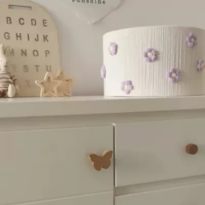 Cómoda branca com puxadores de madeira e objetos decorativos em cima, incluindo candeeiro e painel 'you are my sunshine'.