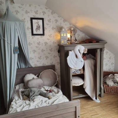Quarto infantil com cama e armário de madeira, almofadas, papel de parede floral e almofada cisne