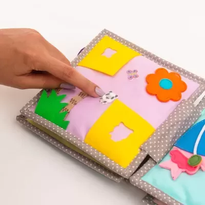 Livro de pano colorido com formas recortadas e flor, para crianças.