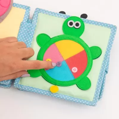 Livro infantil têxtil com tartaruga colorida e mão a tocar botão