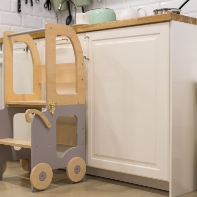 Torre de aprendizagem infantil em madeira e cinza ao lado de armário de cozinha branco