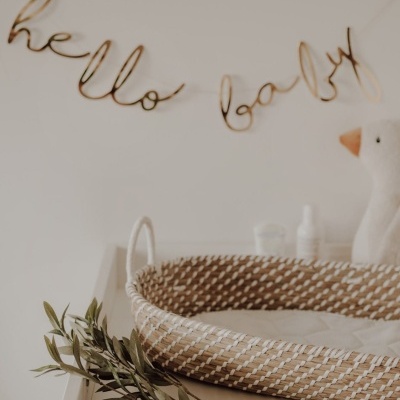 Cesto em fibras naturais com decoração 'hello baby' na parede e boneco de pano