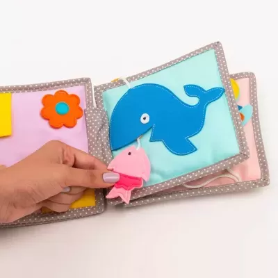 Livro infantil de tecido com baleia azul e peixe rosa em fundo branco