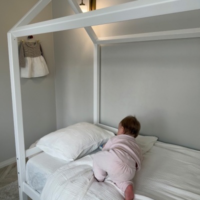 Cama branca de madeira com estrutura de casa e bebé a subir na cama