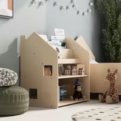 Estante infantil em madeira clara em formato de casa com brinquedos e livros e girafa de pelúcia ao lado num quarto infantil