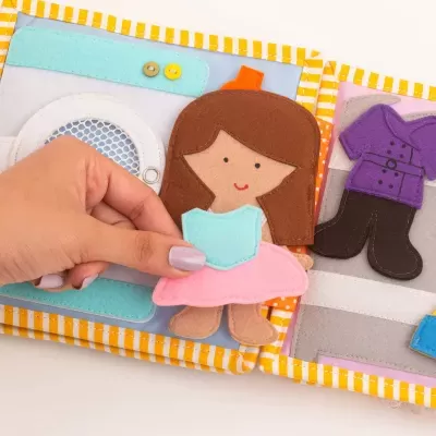 Livro infantil de tecido com personagens e roupas destacáveis