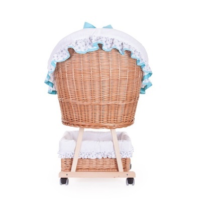 Berço de bebé em verga com base de madeira clara, rodas, almofada e cobertura branca com renda e azul claro