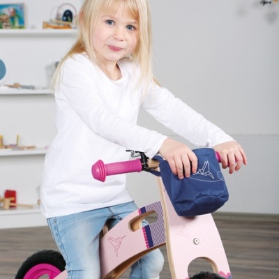 Criança numa bicicleta de equilíbrio cor-de-rosa com bolsa azul no guiador