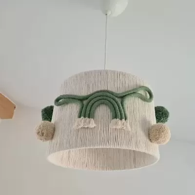 Candeeiro de teto creme com arco-íris em fio verde e bege e pompons, em teto branco com viga de madeira