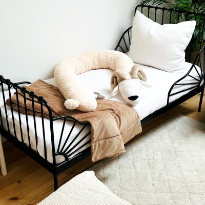 Cama de ferro preta com roupa de cama branca, manta castanha e peluche de animal alongado