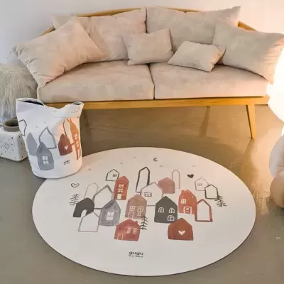 Sofá bege com almofadas e tapete branco com desenhos de casas sobre piso de cimento