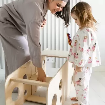 Mulher e criança junto a brinquedo de madeira claro com orifícios circulares