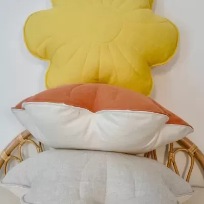 Três almofadas empilhadas em cadeira de palha, incluindo almofada amarela em forma de flor.