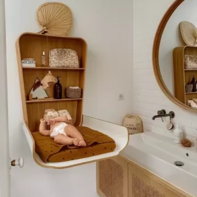 Cama suspensa para bebé com almofada castanha em quarto branco e lavatório com armário em madeira grelha