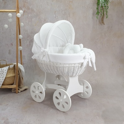 Carrinho de bebé vintage branco em vime com tecto de tecido, almofada e laços, em fundo neutro com decoração