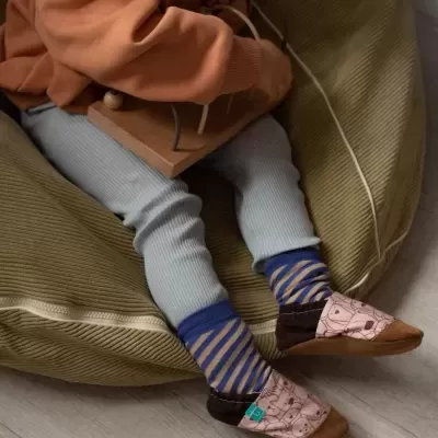 Criança sentada num pufe verde vestindo roupas coloridas e pantufas com padrão.