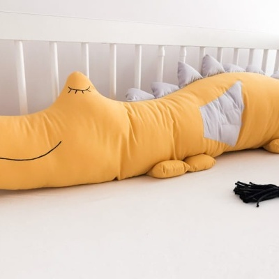 Almofada crocodilo amarelo com detalhes cinzentos sobre colchão branco