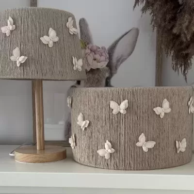 Abajur e cesta cinza com borboletas brancas sobre mesa branca