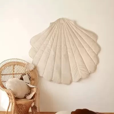 Tapete de parede e almofadas em forma de concha em ambiente com cadeirão de vime e chão de madeira