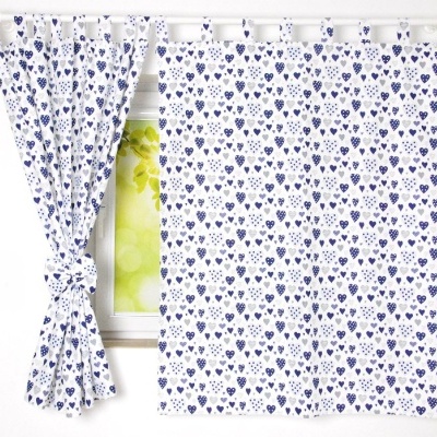 Conjunto de cortinas brancas com corações azuis e cinzentos num ferro branco em frente a uma janela.