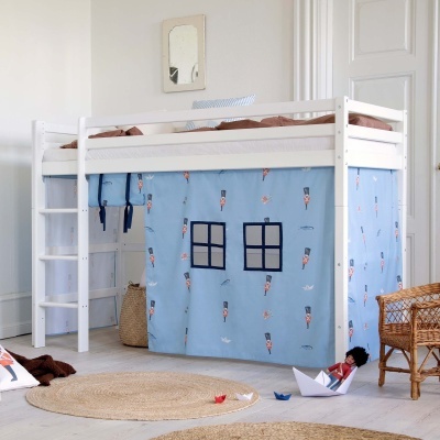 Cama alta infantil branca com cortinas azuis estampadas e acessórios de decoração.