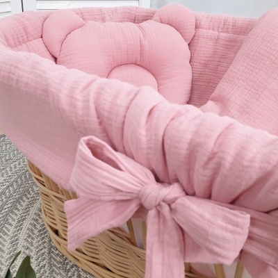 Cesto de vime com forro rosa almofadado e laço decorativo sobre tapete cinza