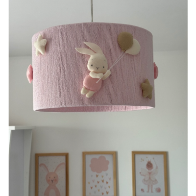 Candeeiro de tecto rosa com coelho em feltro e balões, e três quadros na parede de um quarto.