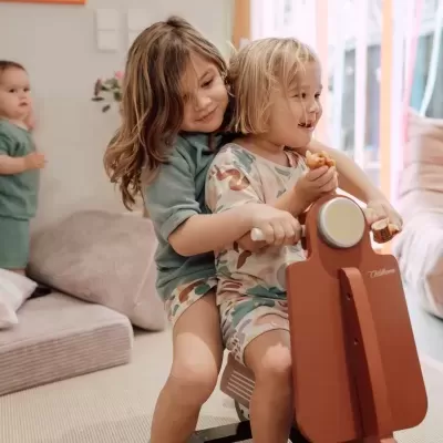 Crianças brincando com moto de balanço vermelha e pantufas com desenhos de animais em espaço interior