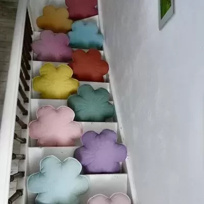 Almofadas flor coloridas dispostas em degraus de escada branca com parede branca ao lado