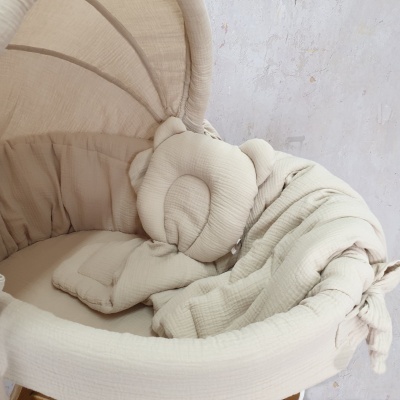 Berço para bebé bege com almofada de cabeça de urso e manta, perto de parede de cor clara