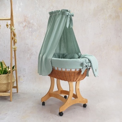 Berço de bebé em vime com tecido verde claro e suporte de madeira com rodízios