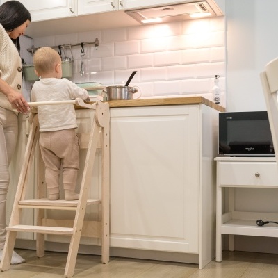 Cozinha branca com pessoa adulta e criança em escadote de madeira na bancada