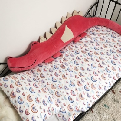 Cama de criança com almofada em forma de crocodilo vermelho e lençol com padrão colorido de arcos