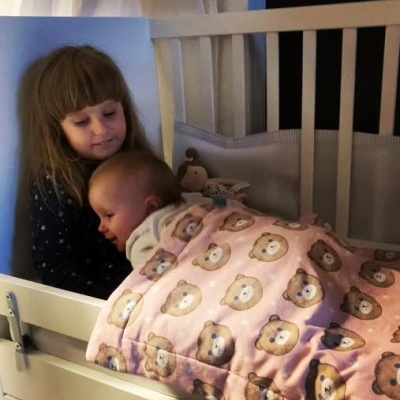 Cobertor rosa com rostos de ursinhos em berço branco com bebé e criança