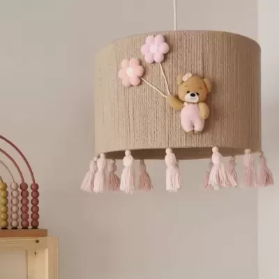 Candeeiro de teto com ursinho e flores cor-de-rosa, franjas cor-de-rosa, e brinquedo de contas coloridas ao lado