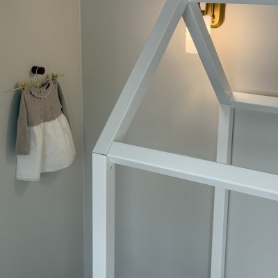 Cama de criança branca estilo casa e vestido infantil cinza e branco pendurado na parede