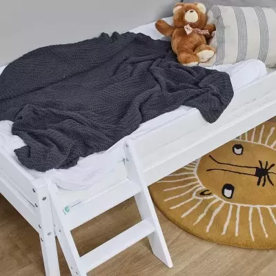 Cama branca de criança com manta cinza, almofada listrada, peluche e tapete de leão amarelo
