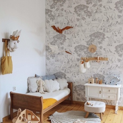 Quarto infantil com cama de madeira, almofadas, tapete cinza, papel de parede com padrão, móveis brancos e brinquedos de madeira