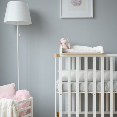 Berço branco em quarto com decoração neutra e quadro com coelho e texto.