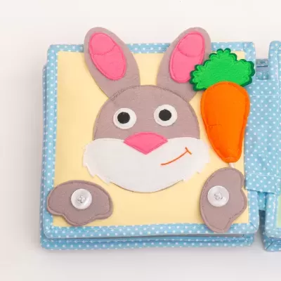 Livro de tecido com capa azul e coelho cinzento e rosa com cenoura de tecido