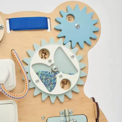 Tabuleiro de madeira com engrenagens azuis e branca com pequenas contas coloridas e fita azul
