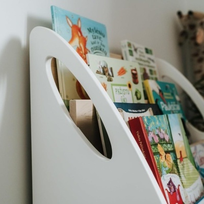 Prateleira branca para livros com livros infantis coloridos e peluche de girafa ao fundo