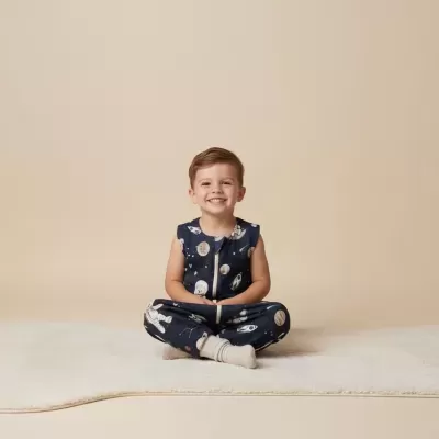 Menino sentado em pijama azul com padrão espacial sorrindo.